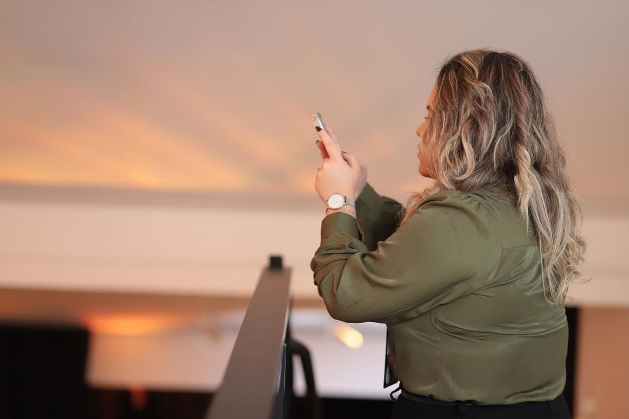 Ana Julia de perfil, de blusa verde-oliva, registrando um evento com o celular