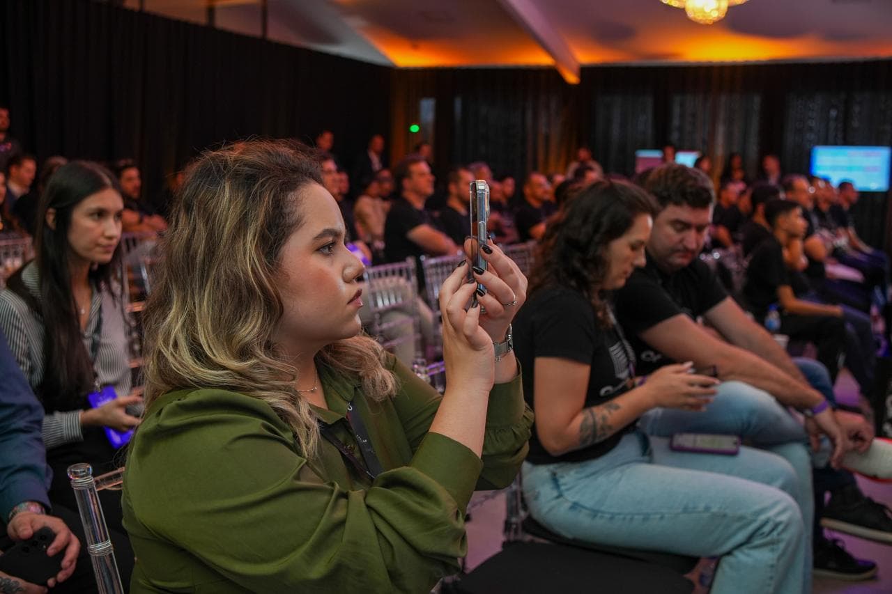 Ana Julia sentada na plateia de um evento, gravando com o celular