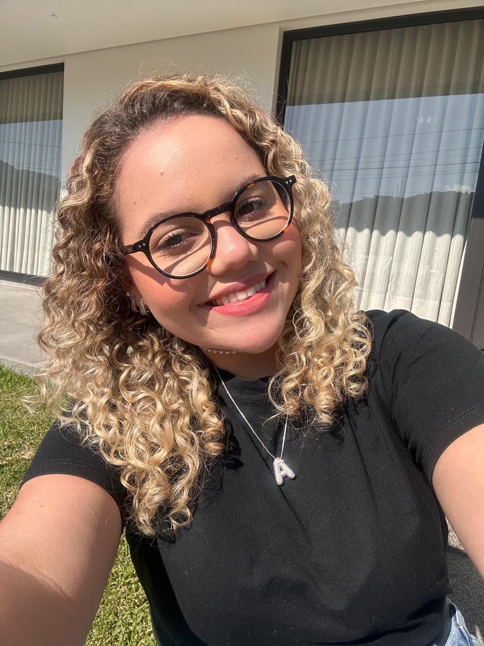 Retrato de Ana Julia sorrindo, de óculos e cabelos cacheados, ao ar livre